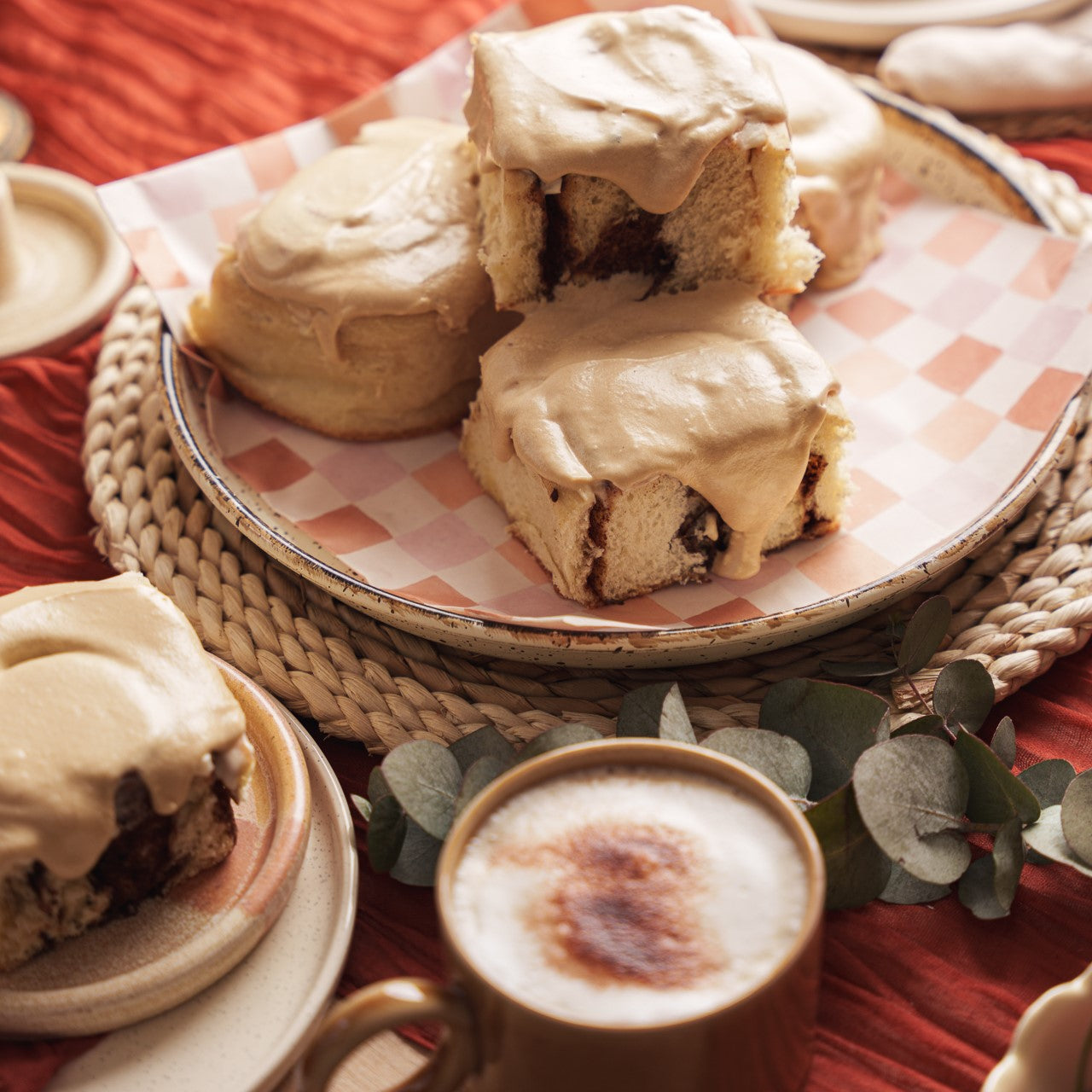Latte Cinnamon buns stacked on a plate with a coffee with frothy milk in the foreground