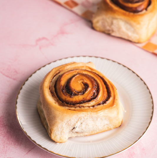 Glazed Cinnamon Buns of Joy bun on a white plate with a pink background
